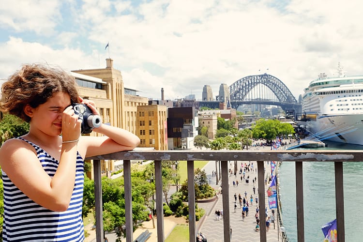 Sydney with Kids, girl holding a photo camera in Sydney, view of cruise ship and Sydney Harbour Bridge