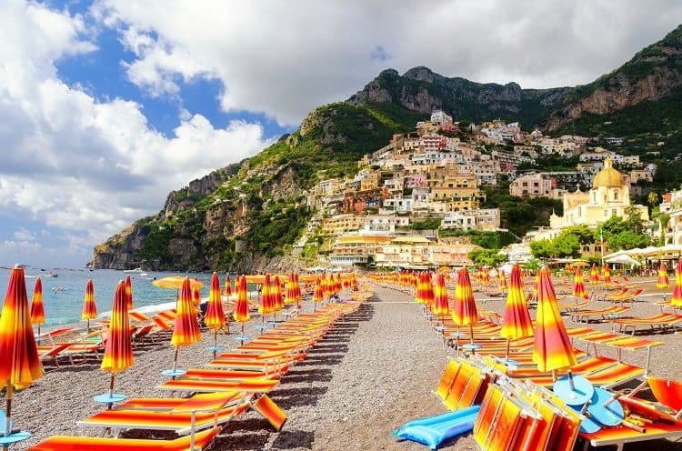 Positano, Amalfi Coast, Italy, photo of the beach, beach sun loungers and umbrellas, colourful buildings in the background, mountains