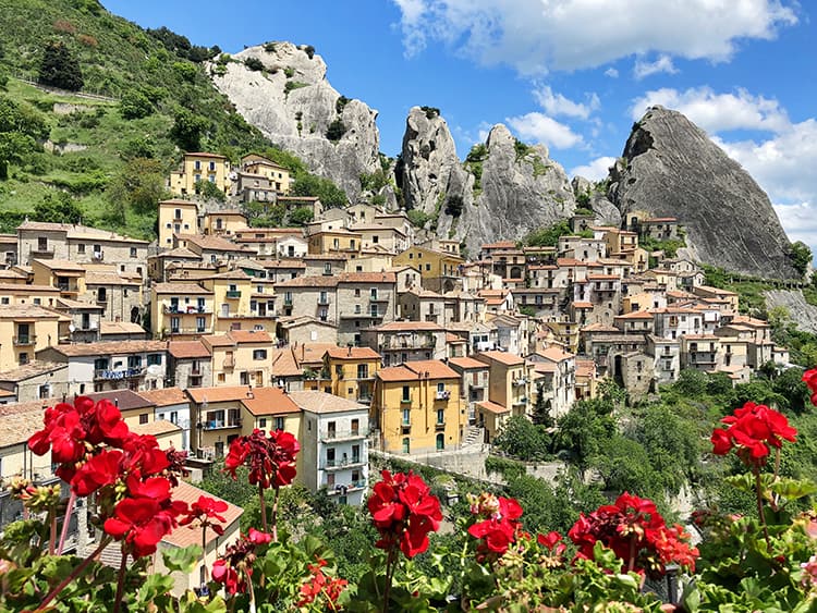 South Italy Cities - Castelmezzano, colourful buildings stacked up on the side of the rocky mountain, red flowers in the foreground