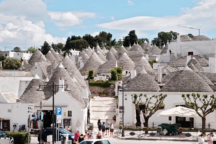 one of the best cities of southern italy - Alberobello, white buildings with grey cone shaped roofs, some people walking around
