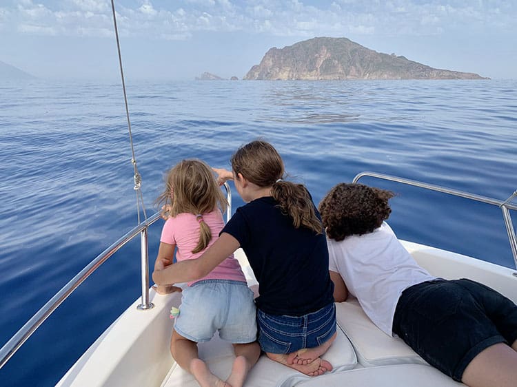 Aeolian Islands, Italy, three daughters looking out towards the islands laying down on the front of the boat