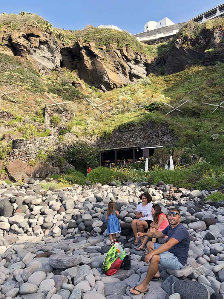 Malfa Beach Salina Island, Italy, rocky beach, father and three daughters siding down on the rocks