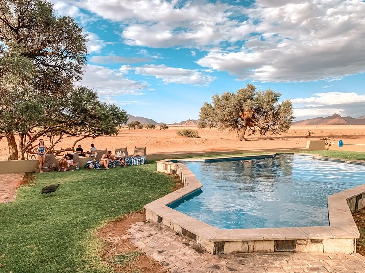 Accommodation in Sossusvlei with Kids - Namibia Travel with Family, family sitting on bean bags next to the pool, desert in background