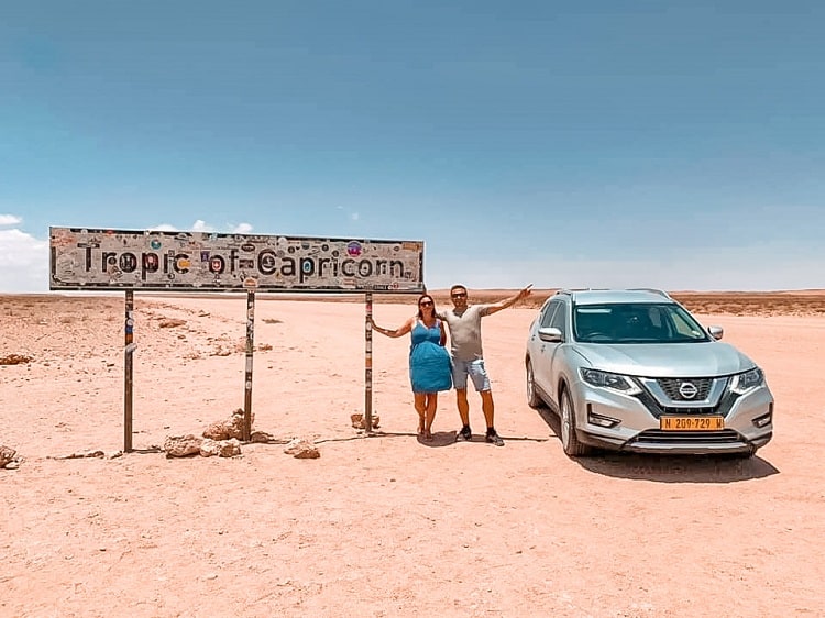 Tropic of Capricorn in Namibia - Driving in Nabia with Kids, a couple posing next to the sign and the car
